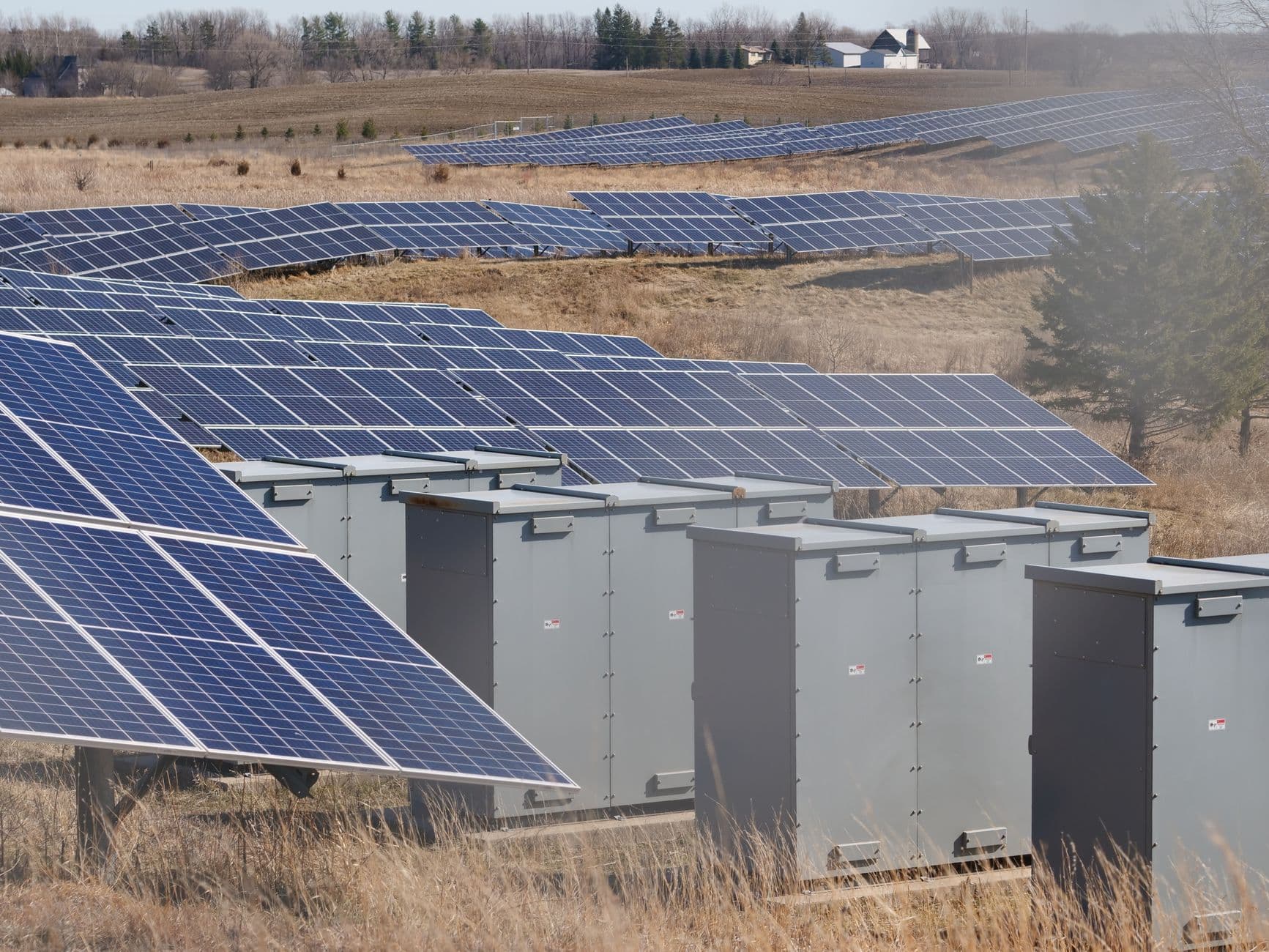 Conteneurs de batteries reliés à un poste électrique et à un parc solaire dans un paysage européen.