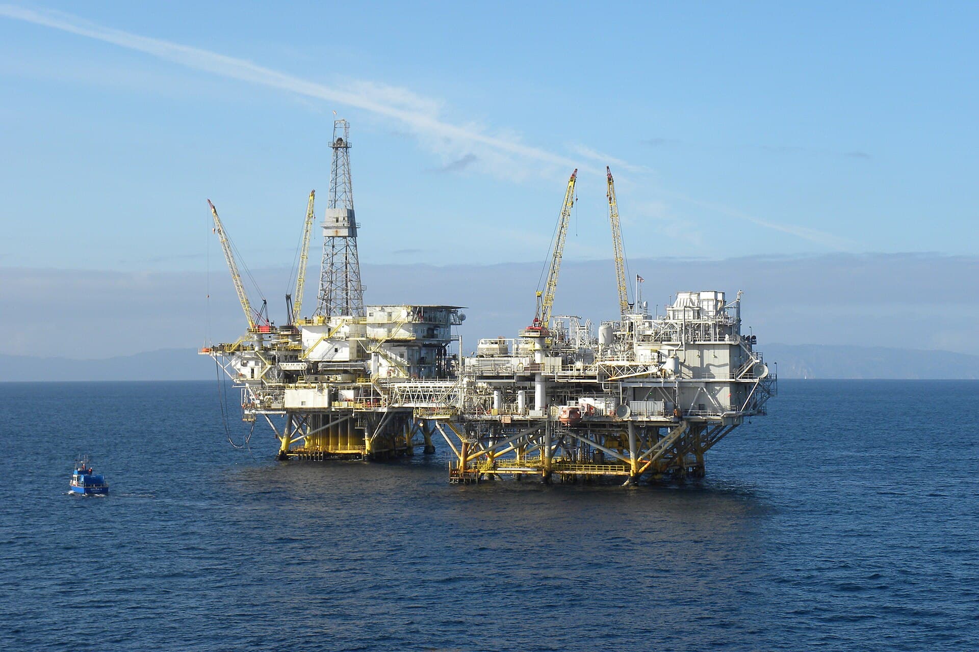 Grande plateforme pétrolière offshore en mer, avec ses conduites, ses grues et un navire de soutien.